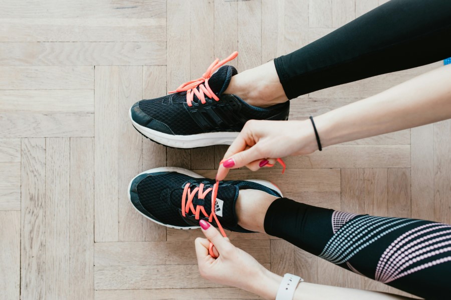 Person tying the laces of black running shoes with bright pink laces, preparing for a run